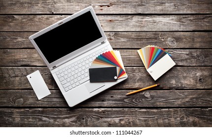 White Laptop With Designer Color Swatches On Old Wooden Table.