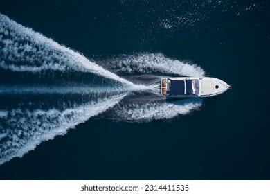 A white large boat with a blue awning is moving fast on dark water, top view. - Powered by Shutterstock