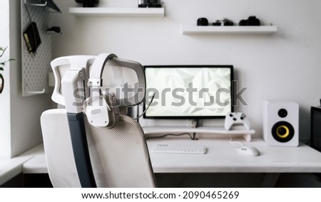 White large gaming headphones with a microphone hang on a white armchair. Close-up