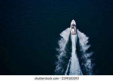 White Large Open Boat With People Moving Fast On Dark Blue Water Top View. White Speedboat Fast Movement On Dark Water Top View. White Speedboat Moving Up Aerial View.