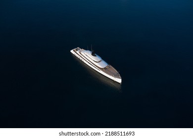 A White Large Super Modern Yacht Stands On Smooth Water In The Morning Rays Of The Sun Aerial View. White Large Modern Yacht On Dark Water Top View.