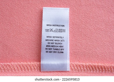 White laundry care washing instructions clothes label on pink cotton shirt - Shutterstock ID 2226595813