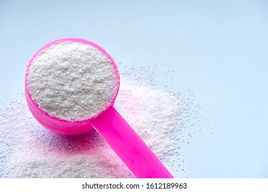 White Laundry Detergent Powder For Washing Machine On Pastel Blue Background And Pink Plastic Scoop For Dosage. Image With Copy Space.                       