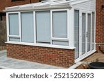 White lean to conservatory with blinds on all windows and doors, seen from the outside on a sunny day. 