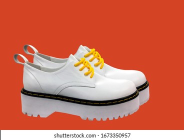 White Leather Platform Shoes Isolated On Red Background. Classic Shoes On A High Black Tractor Platform. Fashionable Strict Low-heeled Shoes. Women Loafers With Lacing. Composition Of Clothes