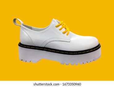 White Leather Platform Shoes Isolated On Yellow Background. Classic Shoes On A High Black Tractor Platform. Fashionable Strict Low-heeled Shoes. Women Loafers With Lacing. Composition Of Clothes