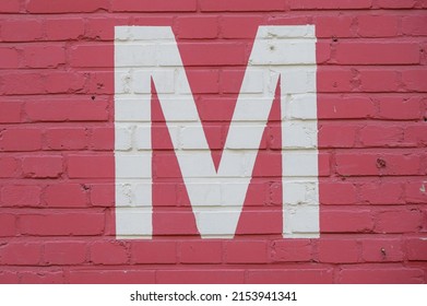 White letter M painted to brick wall on red background (from a letter set containing B, C, D, F, G, M, R and 1, 3, 4)