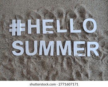 white letters spelling #hellosummer hello summer on sand for a fun beach summer concept 