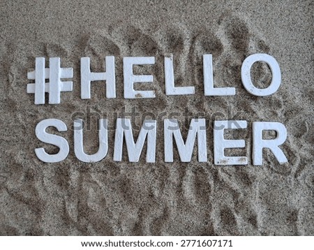 white letters spelling #hellosummer hello summer on sand for a fun beach summer concept 