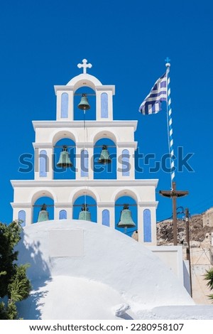 White and light blue bell tower of a church in santorini with greece flag