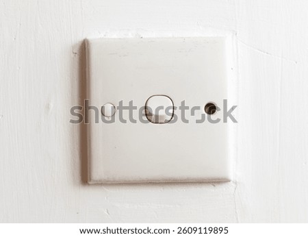 A white light switch is mounted on a wall. The switch is positioned in the center of the wall and is flush with the surface. The switch is turned on, illuminating the area around it