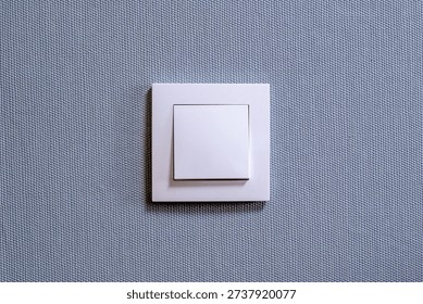 White Light Switch on Square Wall Plate Against Textured Blue Fabric Background for Home Interior