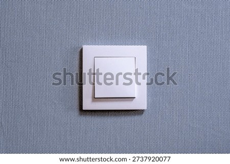 White Light Switch on Square Wall Plate Against Textured Blue Fabric Background for Home Interior