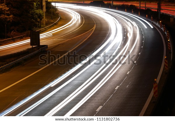 White light trails of cars passing by at high\
speed on the high way. Long exposure picture of white light trails\
of cars on highway.