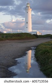 White lighthouse at dusk with its reflection in a puddle of water