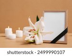 White lily, blank funeral photo frame and candles on beige background