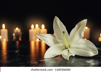 White lily and blurred burning candles on table in darkness, space for text. Funeral symbol - Shutterstock ID 1189306000