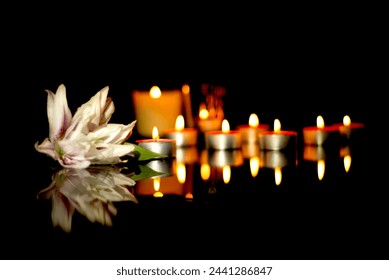 White lily and burning candles In the silence of the darkness of a funeral on a black plaque with the reflection of lights. Sad mourning background - Powered by Shutterstock