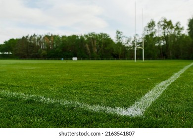 White line marking on a green field with tall goal post for hurling and camogie. National sport of Ireland. Blue cloudy sky. Irish national activity.