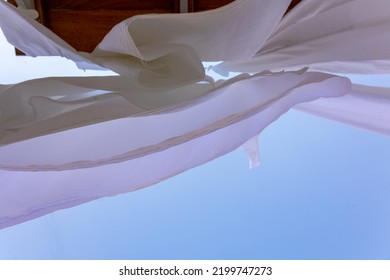 White Linen Drying On Clothesline In Fishing Village Of Symi, Island In Greece. Snow-white Sheets Scatter In Wind. Bottom View. High Quality Photo