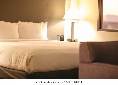 White Lines On A Bed In A Hotel Suite Room In Phoenix, Arizona. Nightstand With A Digital Clock And A Lamp To The Right And A Sofa In Bokeh.