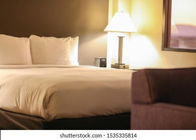 White Lines On A Bed In A Hotel Suite Room In Phoenix, Arizona At Sunrise. Nightstand With A Digital Clock And A Lamp To The Right. Sofa In Bokeh