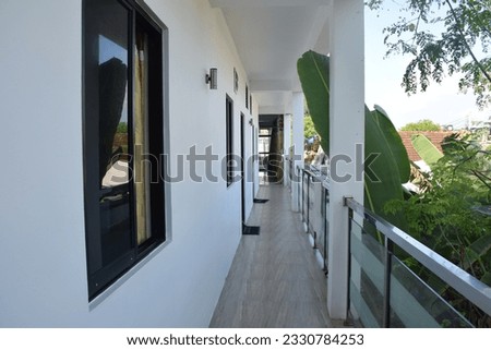 A white long corridor, on one side the doors to the rooms on the other an open veranda and palm trees