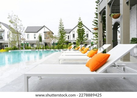 White loungers with orange pillow by swimming pool. Sunbed for sunbathing and swimming pool.