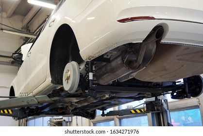 White Luxury Car Raised On A Lift In Service. All Wheels Removed On The Car. Visible Rear Suspension Elements, Rear Beam, Springs, Rear Muffler. 
The Concept Of Quality Car Service.