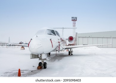 Weißer Luxus-Geschäftsjet in der Nähe des Flugzeughangars bei kältem Winterwetter