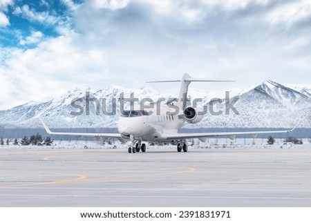 White luxury executive aircraft taxiing on airport taxiway in winter on the background of high scenic snow capped mountains