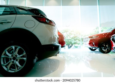 White luxury SUV car parked in modern showroom and blurred red car. Car dealership and auto leasing concept. Automotive industry. Showroom interior. New car stock for sale. Glass building of showroom.