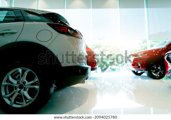 White luxury SUV car parked in modern showroom\
and blurred red car. Car dealership and auto leasing concept.\
Automotive industry. Showroom interior. New car stock for sale.\
Glass building of\
showroom.