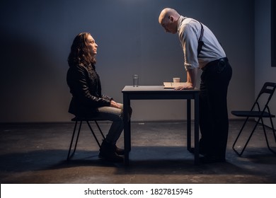 A white male police detective talks to a suspect in a drug trafficking case who is sitting in an interrogation room in handcuffs