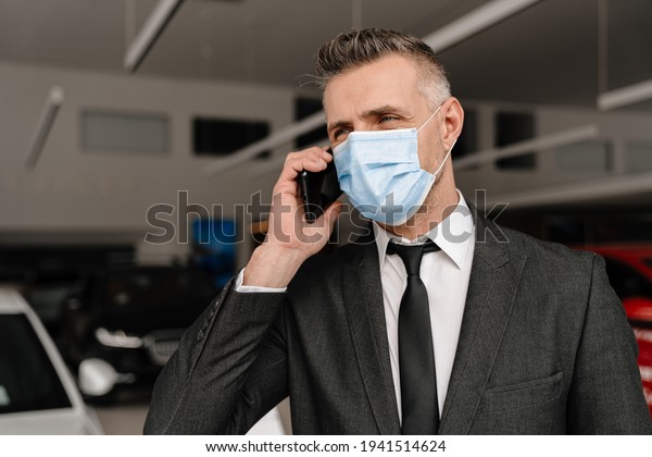 White man in face mask talking on cellphone\
while choosing car at\
showroom