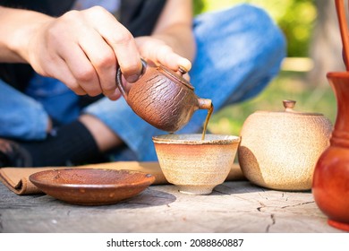 White Man Holding Handmade Ceramic Tea Pot With Tea Set On Stump In City Park