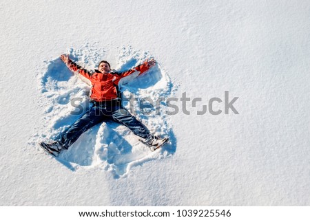 A white man lies serenity on the snow and flapping his arms and legs in different directions like snow angel. Toned image.