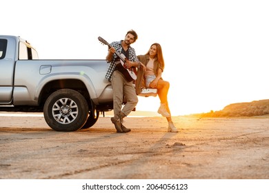 White man playing guitar during travel on car with his girlfriend outdoors - Powered by Shutterstock