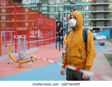 White Man In Protective Mask Standing Behind Tape Fenced Outdoor Gym. Covid 19 Quarantine Restrictions.