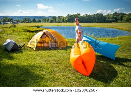 White man setting up inflatable sofas out in the wild camping