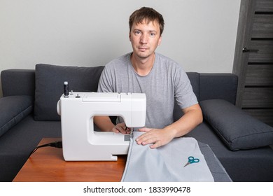 White Man Sews Fabric On A Sewing Machine. Home Sewing And Needlework During The Covid-19 Pandemic. Production Of Covers And Clothes. 