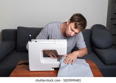 White Man Sews Fabric On A Sewing Machine. Home Sewing And Needlework During The Covid-19 Pandemic. Production Of Covers And Clothes. 