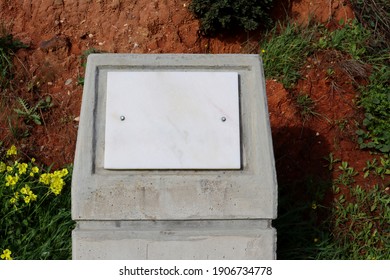 White Marble  Board On A Stone Plinth, Surrounded By Green Plants And Soil.