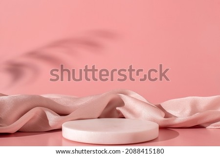White marble podium on the pink background with silk fabric and shadow of tropical plant. Podium for product, cosmetic presentation. Creative mock up. Pedestal or platform for beauty products.