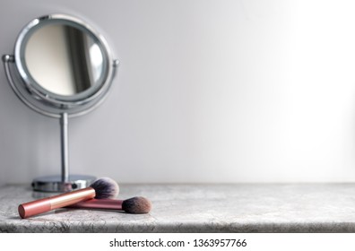 White marble table top can used for display or montage your products. Selective focus blurred white background. Vanity table with makeup brushes and  mirror. 