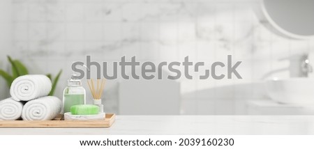 White marble table top with hand towels, soap, shampoo, aroma diffuser in wood tray and mockup space for montage product over blurry bright marble bathroom interior, 3d rendering, 3d illustration