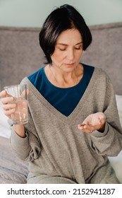 White Mature Woman Taking Medicine While Sitting On Bed At Home