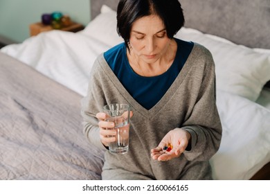 White Mature Woman Taking Medicine While Sitting On Bed At Home