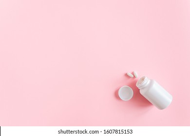 White medical bottle and two pills dietary supplements, nutraceuticals, antibiotic, painkillers on pink background. Health and drug treatment concept. Top View Copy Space.