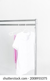 White Medical Doctor Or Physician Lab Coats With Pink Pants Hanging On Clothes Mobile Grey Hangers With Wheels, On White Background. Copy Space, Selected Focus. Vertical Picture.